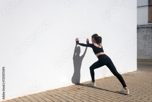 Fotografija sporty woman doing hamstring stretch against a white wall