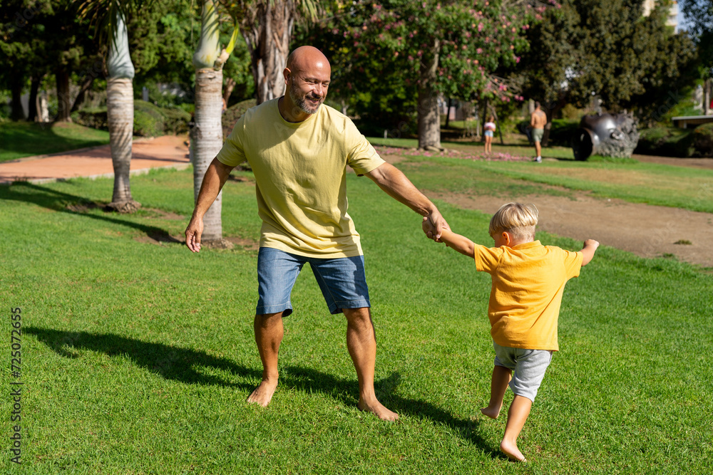 father and son spinning in the park. dad and son play barefoot on the green lawn. positive family photo of father and son father and son spinning in the park. dad and son play barefoot on the green lawn. positive family photo of father and son
