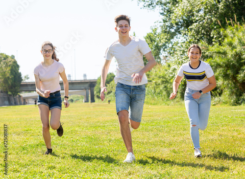 Group of cheerful teenagers running together in summer city park. Happy healthy adolescence concept