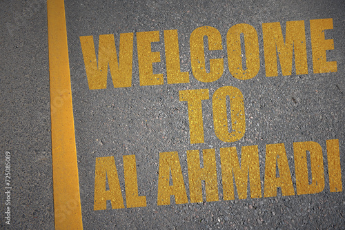 asphalt road with text welcome to Al Ahmadi near yellow line. photo