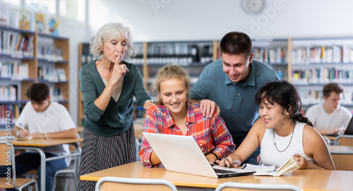 Mature European teacher woman asks amused schoolchildren to behave a little quieter, who are preparing for classes in the school library