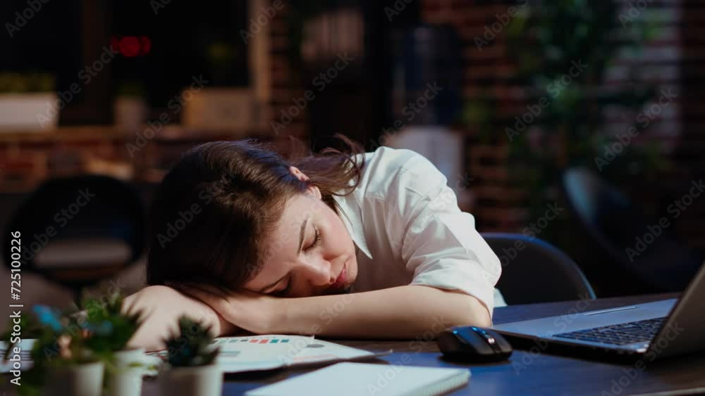 Sleepy employee asleep on computer desk late at night in brick wall office. Panning shot of tired businesswoman sleeping with head on table while working overnight on laptop, camera B Sleepy employee asleep on computer desk late at night in brick wall office. Panning shot of tired businesswoman sleeping with head on table while working overnight on laptop, camera B