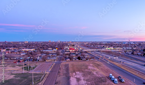 Aerial Cityscape of Lubbock Texas with traffic on the roads and tall buildings in the background against a blue sky at sunrise.