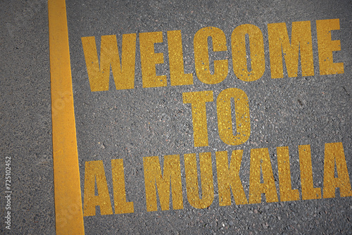 asphalt road with text welcome to Al Mukalla near yellow line. photo