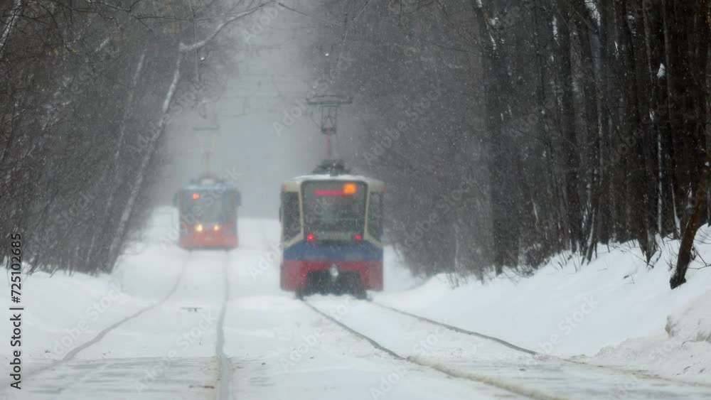 Two trams drive by railroad among trees during snowfall at winter day Two trams drive by railroad among trees during snowfall at winter day
