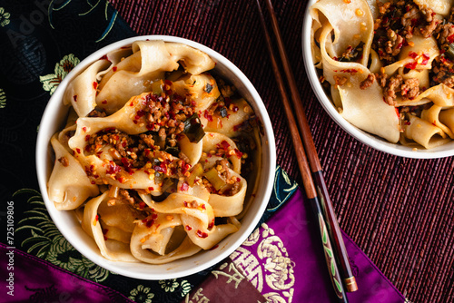 Bowls of Biang Biang Noodles Topped with Spicy Chili Oil Sauce: Biang biang mian topped with minced pork and chili oil served in bowls with chopsticks