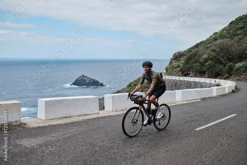 A cyclist is riding a mountain road on a gravel bike.A male cyclist is cycling in the mountains with view on ocean on Tenerife, Canary Island, Spain. Man cyclist wearing cycling kit and helmet.