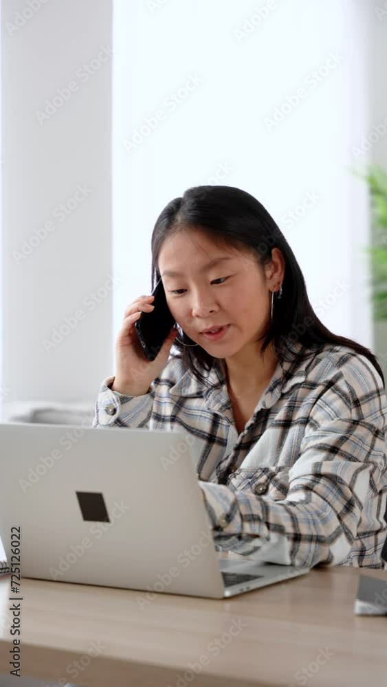 Young asian woman working from home. Person using laptop while talking on phone. Young asian woman working from home. Person using laptop while talking on phone.