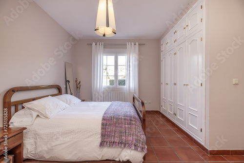 A bedroom with a white duvet with cushions on a wooden double bed next to the window