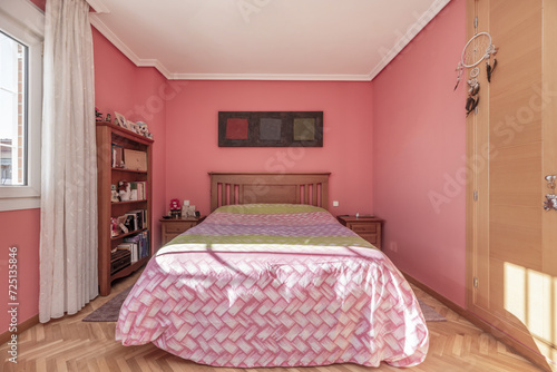 A large bedroom with a pink quilt on the bed with a wooden headboard and side tables