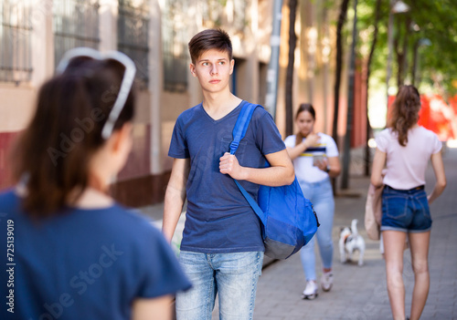 Confident teen boy with backpack strolling through modern city streets on sunny summer day