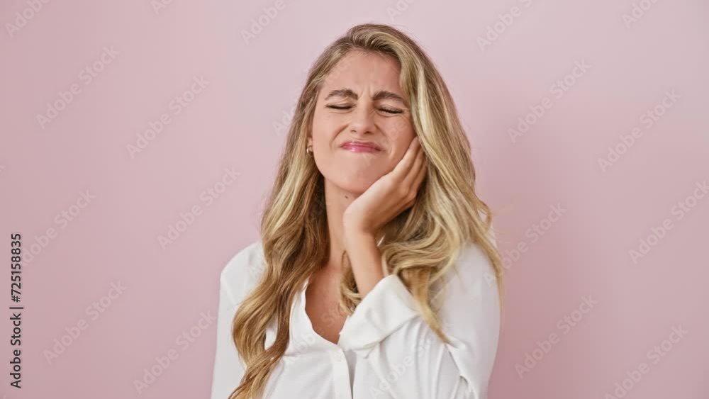 Blonde young woman in shirt reacts to severe tooth ache, touches mouth with hand, standing over pink isolated background, dental illness evident Blonde young woman in shirt reacts to severe tooth ache, touches mouth with hand, standing over pink isolated background, dental illness evident