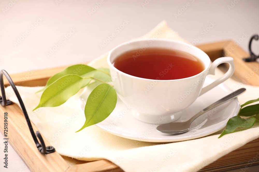 Aromatic tea in cup, saucer, spoon and green leaves on table Aromatic tea in cup, saucer, spoon and green leaves on table