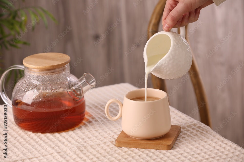 Woman pouring milk into cup with aromatic tea at table, closeup Woman pouring milk into cup with aromatic tea at table, closeup