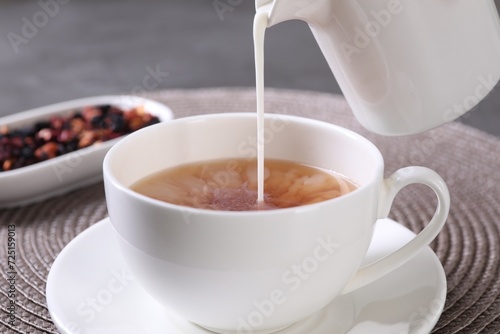 Pouring milk into cup with aromatic tea at table, closeup