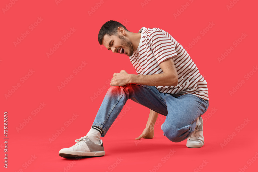 Young man feeling pain in knee on red background