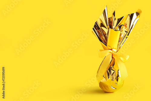 Chocolate Easter egg wrapped in golden foil on yellow background photo