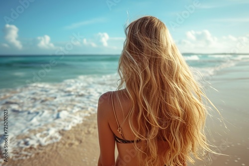 An attractive young blond woman with beautiful long hair on a sandy beach in the . back view.