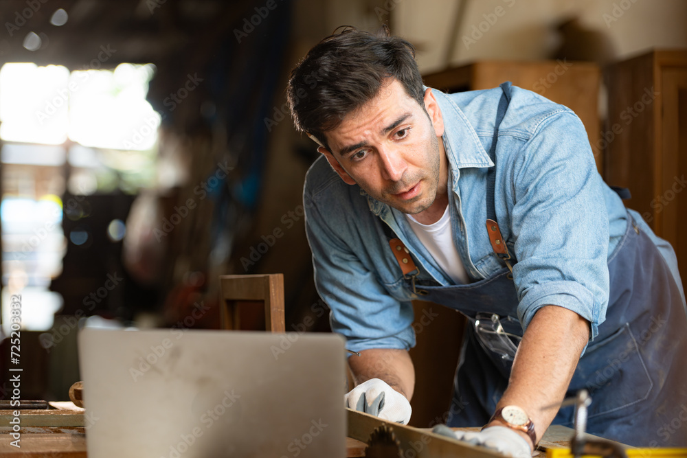 Carpenter working on laptop in his workshop at a woodworking factory Carpenter working on laptop in his workshop at a woodworking factory