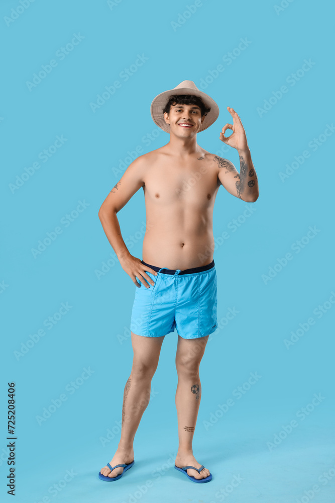 Young man in summer hat showing OK on blue background