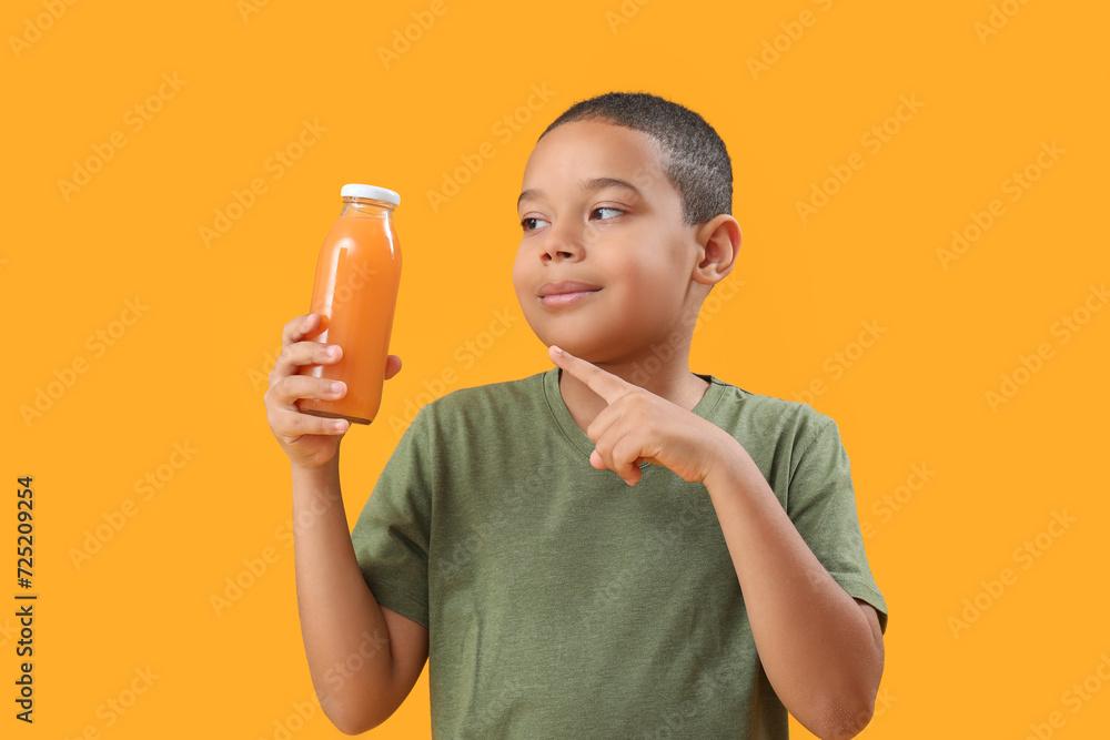 Little African-American boy pointing at bottle of orange juice on color background Little African-American boy pointing at bottle of orange juice on color background
