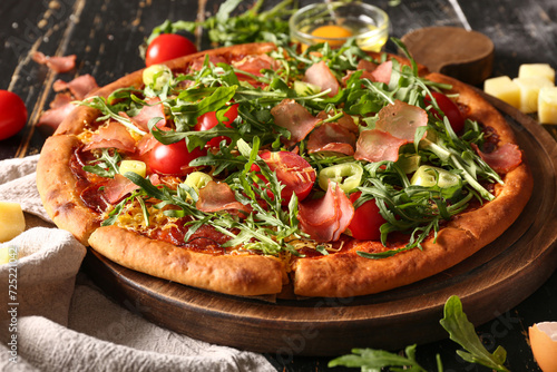 Картината върху платно Board of delicious pizza with tomatoes and arugula on black wooden background
