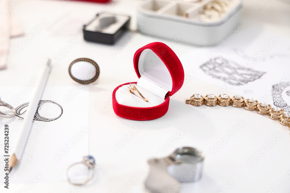 Sketches of stylish accessories with tools and engagement ring on jeweler table in workshop Sketches of stylish accessories with tools and engagement ring on jeweler table in workshop