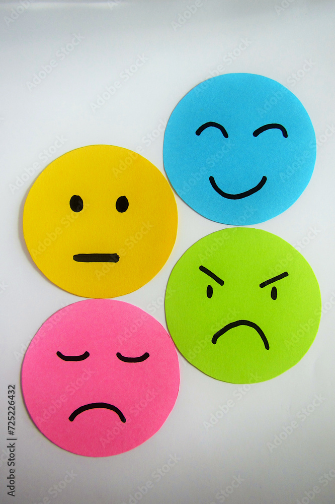 Fototapeta premium Different moods on yellow, blue, pink and green paper faces. Concept of emotions on white background.