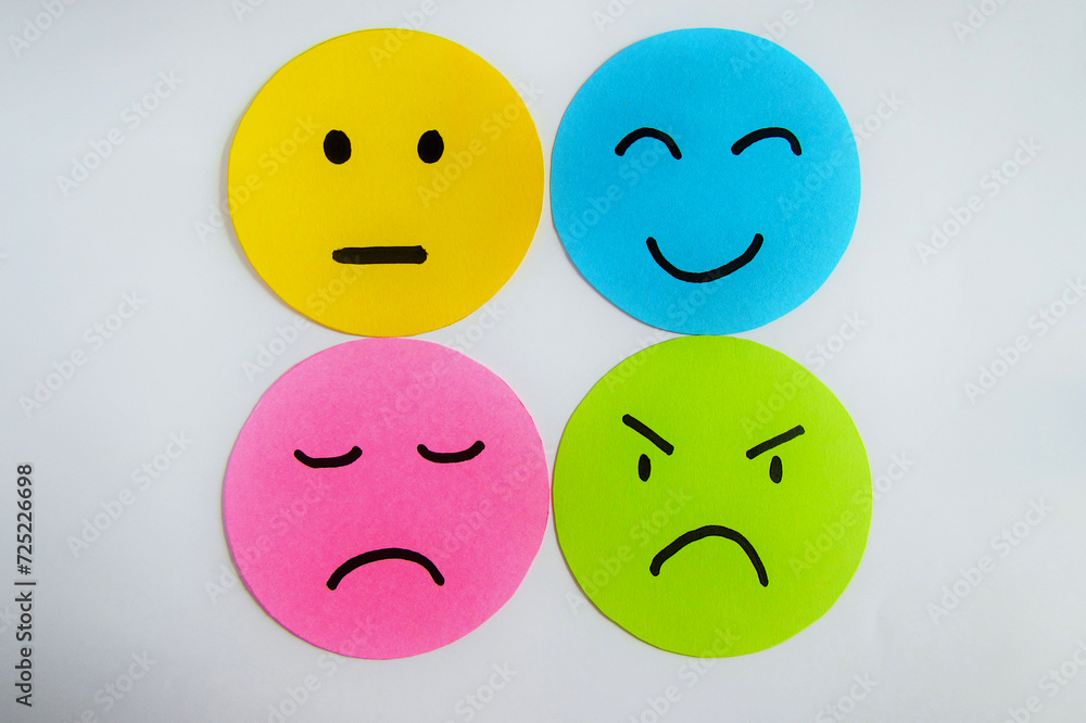 Fototapeta premium Different moods on yellow, blue, pink and green paper faces. Concept of emotions on white background.