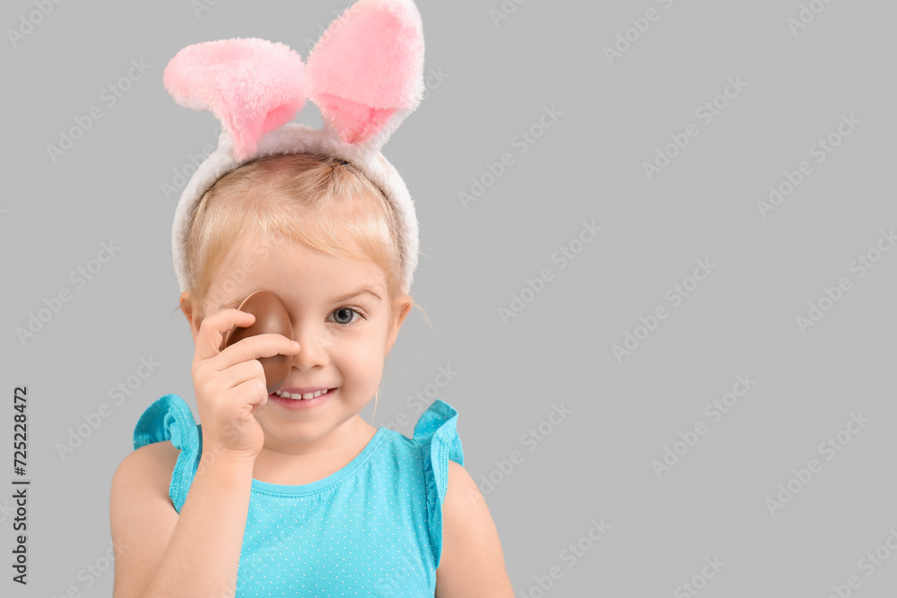 Happy little girl in bunny ears with chocolate egg on grey background. Easter celebration Happy little girl in bunny ears with chocolate egg on grey background. Easter celebration