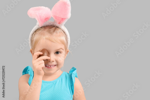 Happy little girl in bunny ears with chocolate egg on grey background. Easter celebration