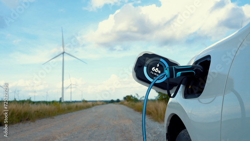 Electric car recharging energy from EV charging station display futuristic smart battery status hologram by EV charger plug cable in wind turbine farm. Alternative clean energy sustainability. Peruse