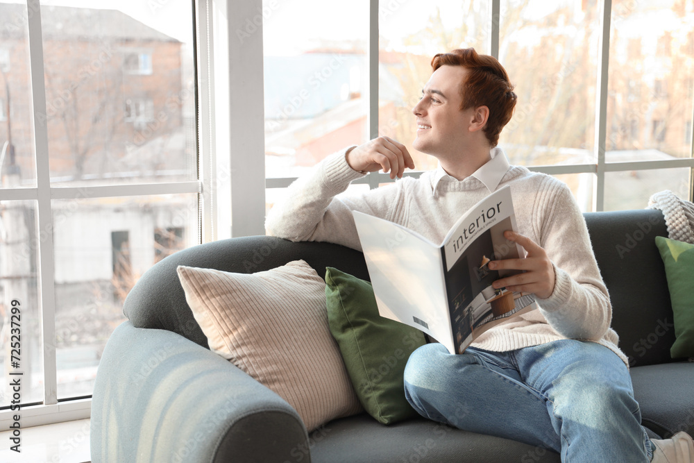 Young man reading magazine on soft sofa near window in living room Young man reading magazine on soft sofa near window in living room