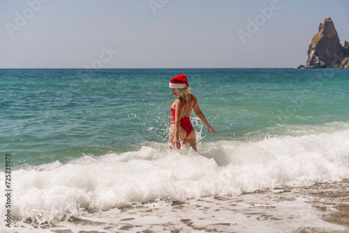 A woman in Santa hat on the seashore, dressed in a red swimsuit. New Year's celebration in a hot country © svetograph
