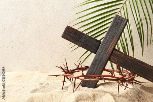 Wooden cross with palm leaf and crown of thorns on sand photo