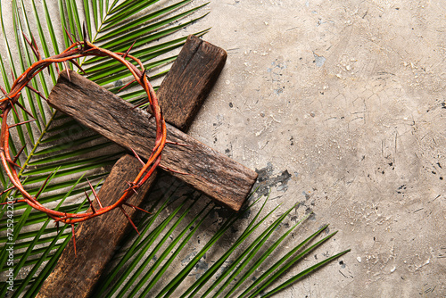 Wooden cross with palm leaves and crown of thorns on grey background