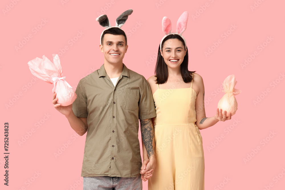 Happy young couple with Easter gifts and bunny ears on pink background Happy young couple with Easter gifts and bunny ears on pink background