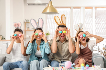 Happy family in bunny ears with painted eggs sitting at home on Easter Day