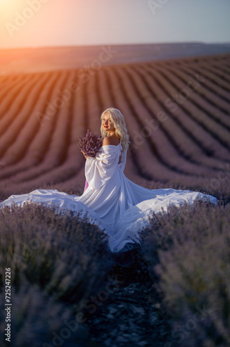 Blonde woman poses in lavender field at sunset. Happy woman in white dress holds lavender bouquet. Aromatherapy concept  lavender oil  photo session in lavender