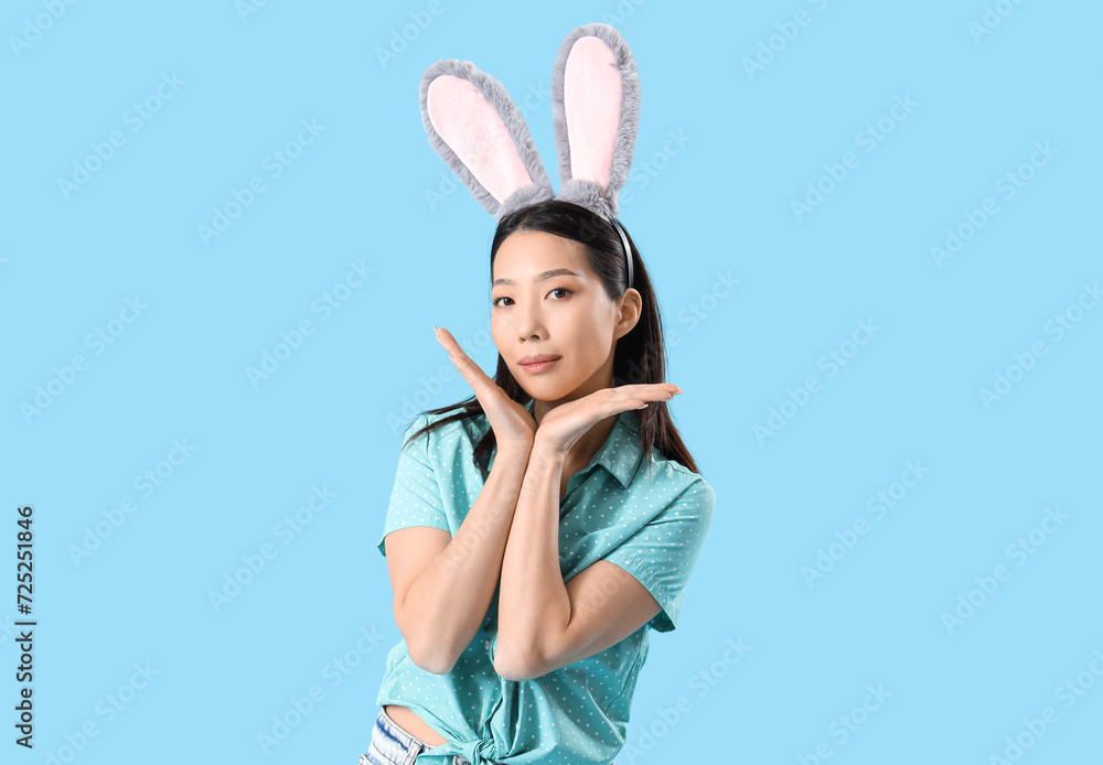 Young Asian woman in bunny ears on blue background. Easter celebration