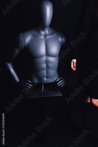 Fototapeta Naklejka Na Ścianę i Meble -  woman dressed in short black dress with black leather boots posing with male mannequin torso