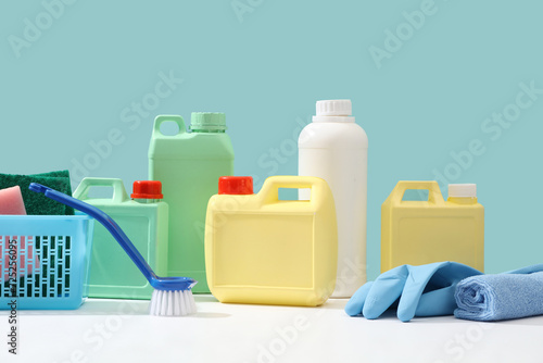 Cleanliness concept for advertising product. Front view of yellow, green and white plastic canisters decorated with blue cleaning equipment on pastel blue background. Minimal scene, space for design