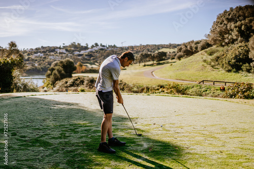 Sotogrante, Spain - January 25, 2024 - Golfer in mid-swing on tee box with golf ball in the air, scenic backdrop with trees and path.