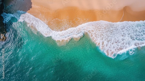  an aerial view of a beach with a wave coming in and a person standing on a surfboard in the water.
