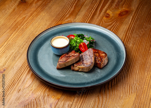 Grilled beef tongue in a plate on a wooden background