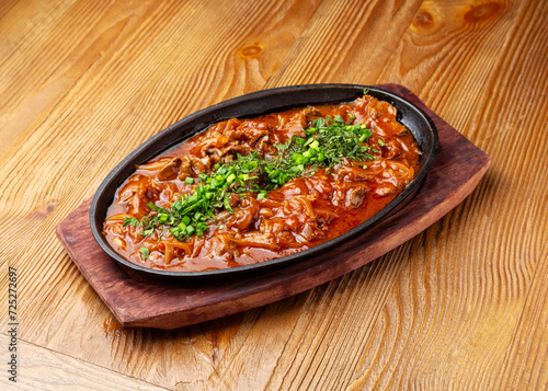 Beef in sauce in a frying pan on a wooden background