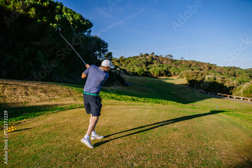 Sotogrante, Spain - January 25, 2024 - Man mid-swing at a golf ball on a course with trees and a clear sky.