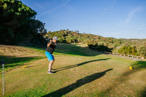 Sotogrante, Spain - January 25, 2024 - Man swinging a golf club on tee off area with grass and trees in background...