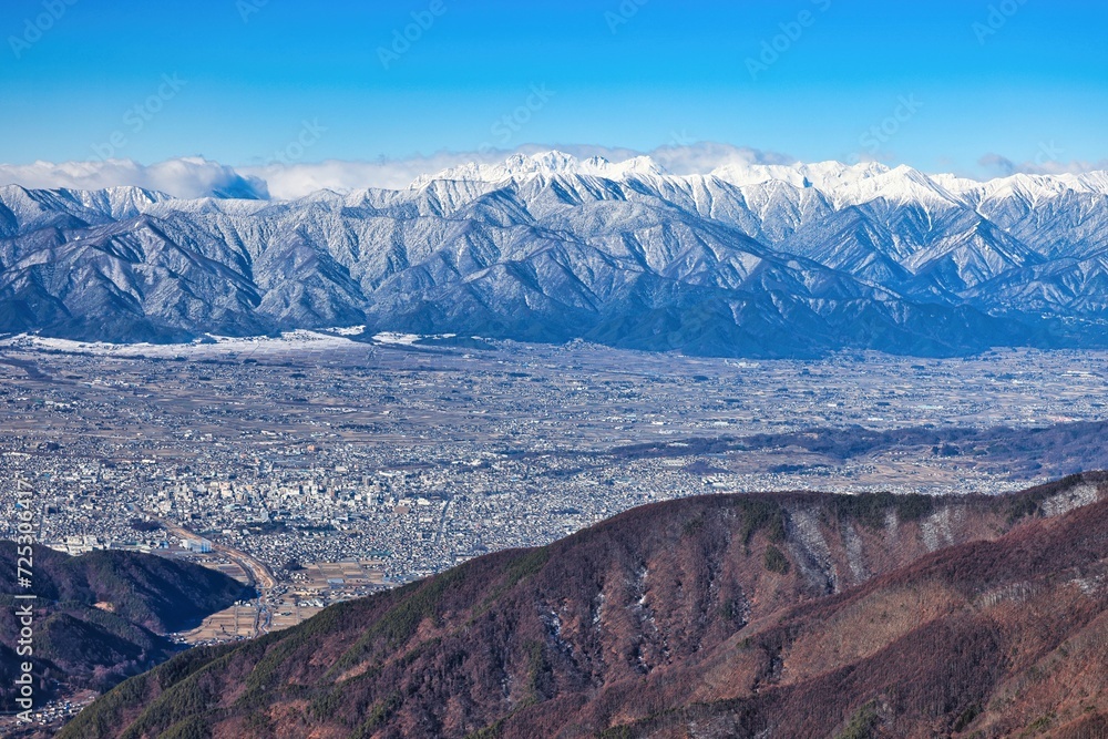 冠雪の北アルプスの穂高連峰と長野県松本市の街並み