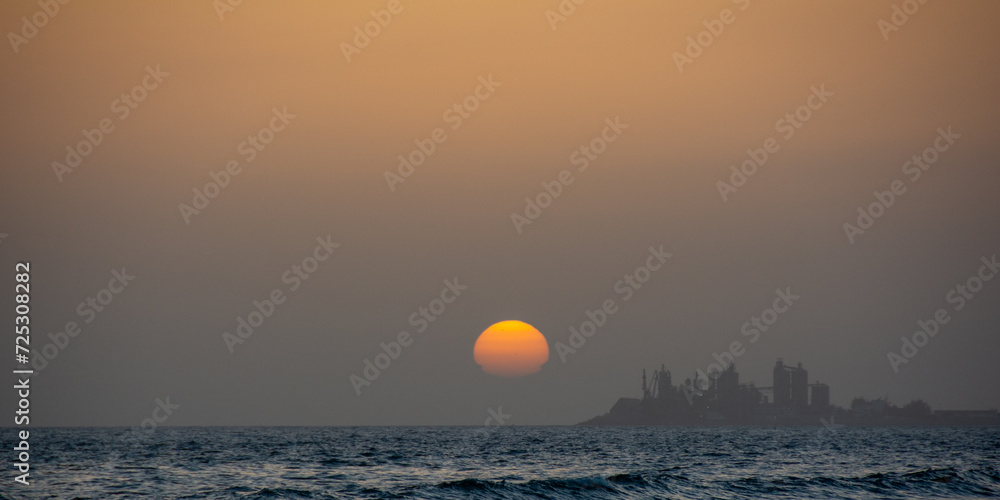 Obraz premium Sunset over the sea with a city in silhouette